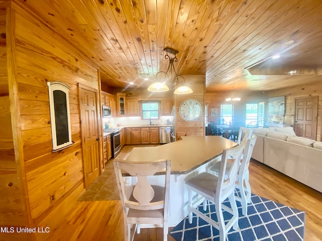 kitchen featuring light hardwood / wood-style flooring, appliances with stainless steel finishes, an inviting chandelier, and wooden walls