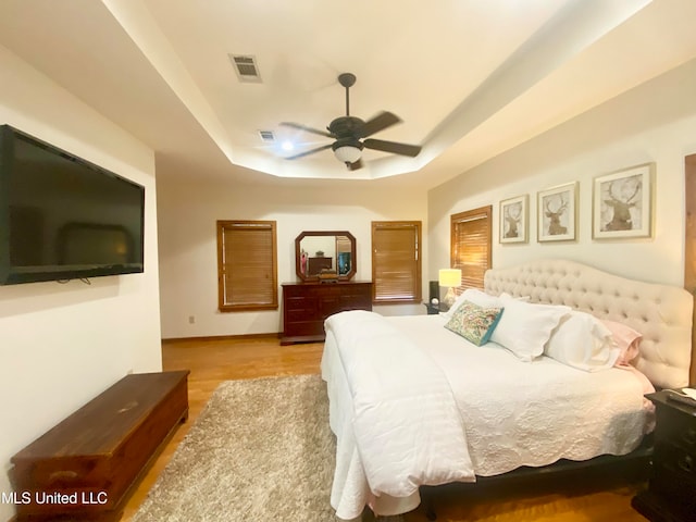 bedroom with light hardwood / wood-style flooring, a tray ceiling, and ceiling fan