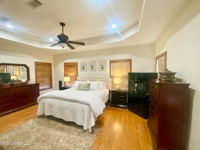 bedroom with a tray ceiling, light hardwood / wood-style floors, and ceiling fan