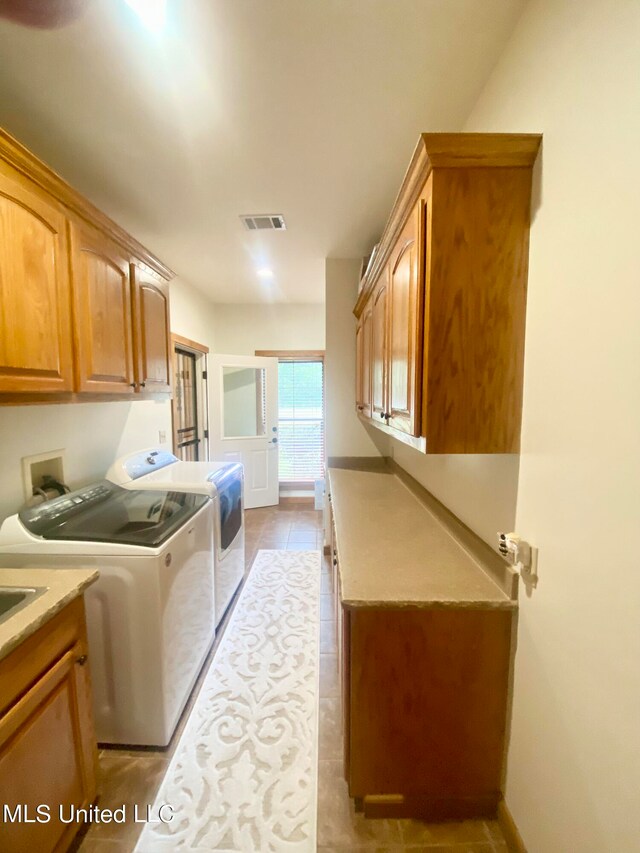 clothes washing area featuring independent washer and dryer, light tile patterned flooring, and cabinets