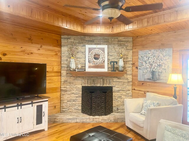 living room with light wood-type flooring, a stone fireplace, ceiling fan, wooden ceiling, and wooden walls