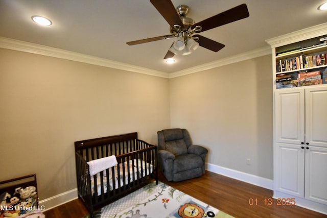 bedroom with a nursery area, ceiling fan, crown molding, and dark wood-type flooring