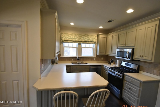 kitchen featuring kitchen peninsula, a breakfast bar, tasteful backsplash, appliances with stainless steel finishes, and sink