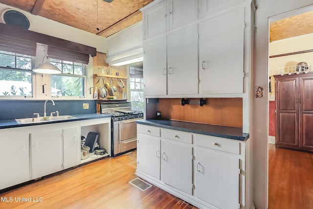 kitchen featuring light wood finished floors, dark countertops, gas stove, white cabinetry, and a sink