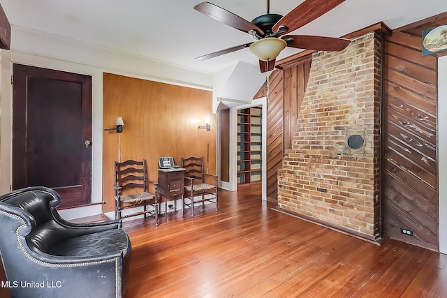 living area featuring brick wall, hardwood / wood-style floors, wood walls, and a ceiling fan