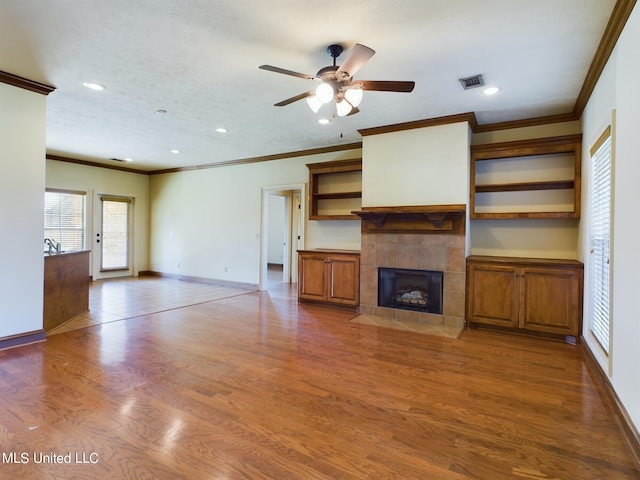 unfurnished living room featuring ceiling fan, wood-type flooring, ornamental molding, and a tiled fireplace