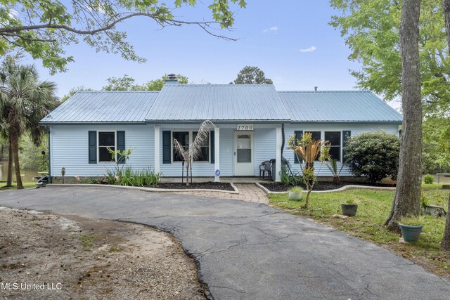 ranch-style house featuring a porch, driveway, metal roof, and a chimney