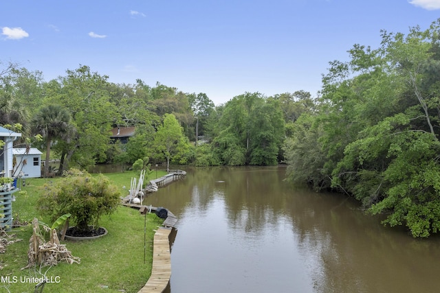 dock area with a lawn, a water view, and a view of trees