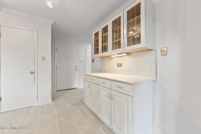 kitchen featuring ornamental molding, white cabinets, light tile patterned floors, and backsplash