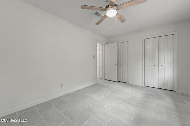 unfurnished bedroom with ceiling fan, multiple closets, and light tile patterned floors