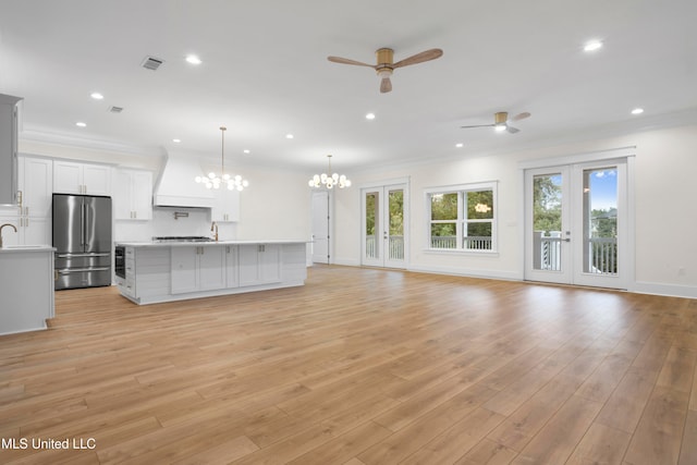 unfurnished living room with french doors, crown molding, light wood-type flooring, and ceiling fan with notable chandelier