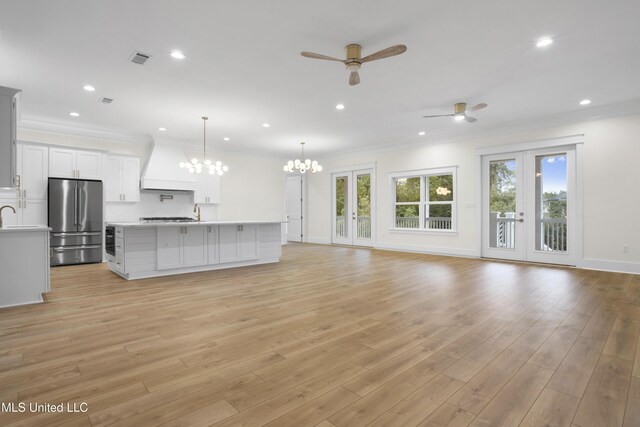 unfurnished living room with ornamental molding, ceiling fan with notable chandelier, light wood-type flooring, and visible vents