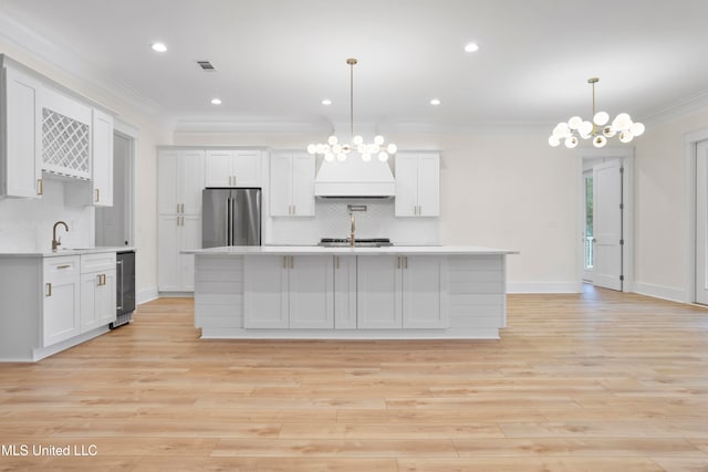 kitchen featuring stainless steel fridge, white cabinets, hanging light fixtures, and light wood-type flooring