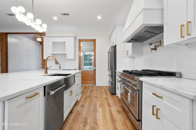 kitchen with high end appliances, decorative light fixtures, custom exhaust hood, white cabinetry, and light hardwood / wood-style floors