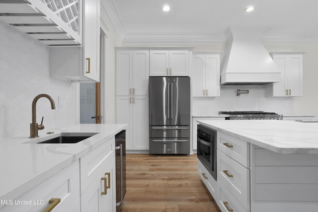 kitchen featuring light wood finished floors, a sink, white cabinets, appliances with stainless steel finishes, and custom exhaust hood
