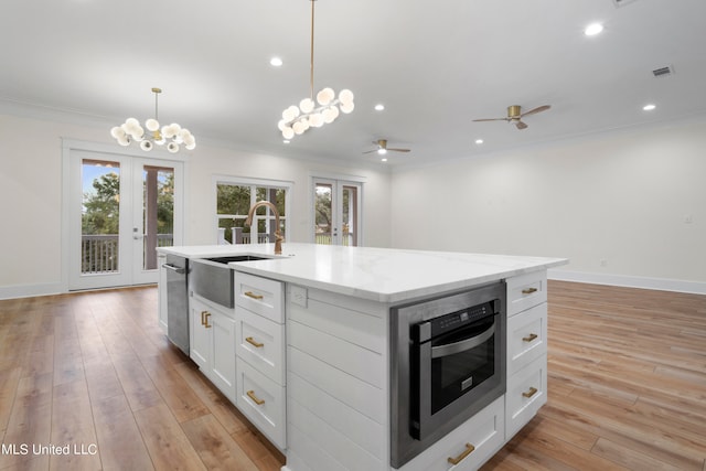 kitchen featuring white cabinetry, french doors, light hardwood / wood-style flooring, and an island with sink