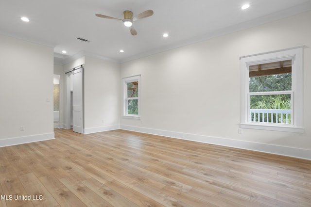 unfurnished room with visible vents, a barn door, ceiling fan, light wood-style floors, and ornamental molding