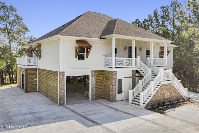 raised beach house featuring covered porch, a carport, concrete driveway, a shingled roof, and stairs