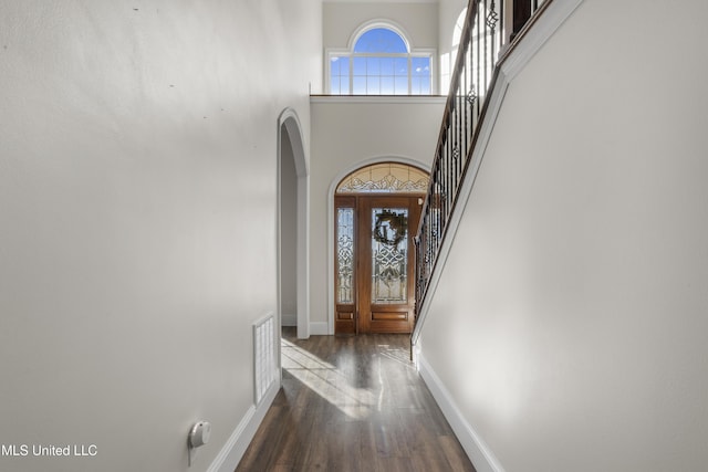 interior space featuring arched walkways, wood finished floors, baseboards, a high ceiling, and stairs