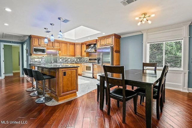 kitchen with a kitchen island, dark hardwood / wood-style floors, wall chimney exhaust hood, hanging light fixtures, and appliances with stainless steel finishes