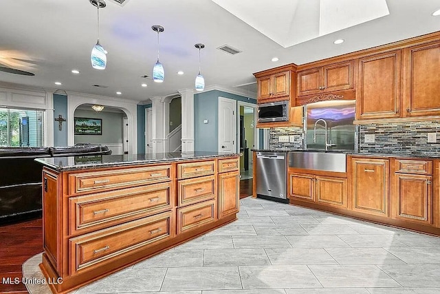 kitchen with a center island, stainless steel appliances, hanging light fixtures, and decorative columns