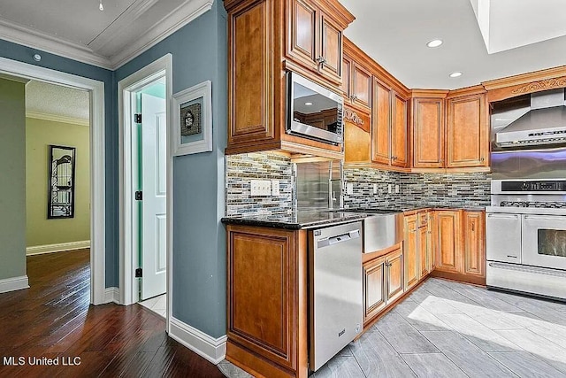 kitchen featuring wall chimney exhaust hood, stainless steel appliances, backsplash, crown molding, and light wood-type flooring