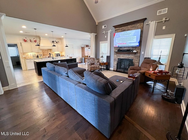 living room with high vaulted ceiling, decorative columns, a fireplace, ornamental molding, and wood-type flooring