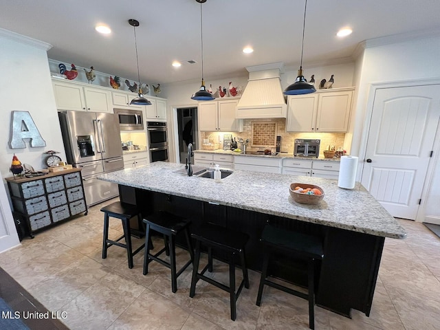 kitchen featuring premium range hood, appliances with stainless steel finishes, sink, hanging light fixtures, and a center island with sink