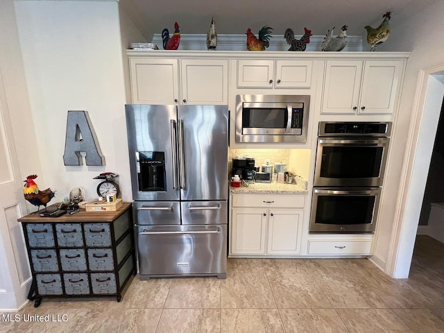 kitchen with appliances with stainless steel finishes, white cabinets, light stone counters, and decorative backsplash