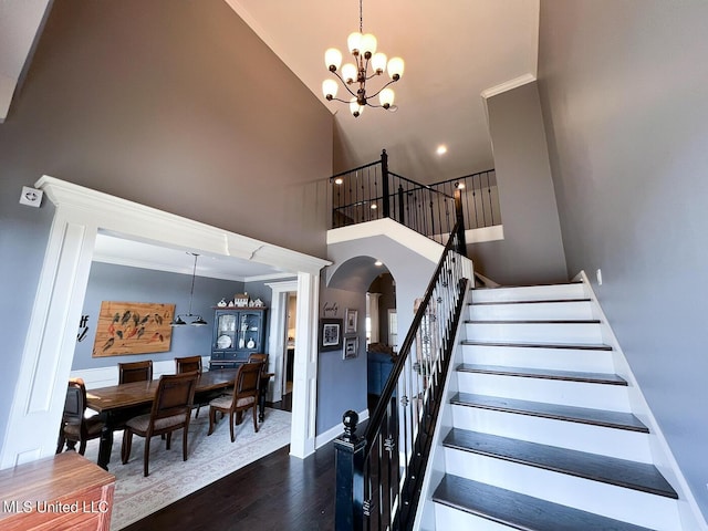 stairway featuring wood-type flooring, a towering ceiling, a chandelier, and crown molding