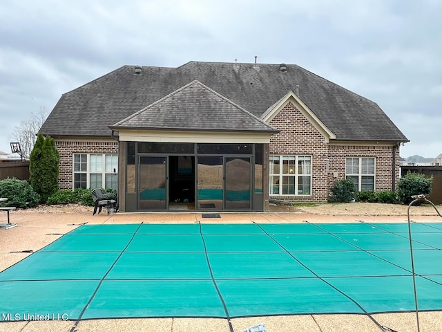 rear view of property featuring a sunroom, a patio, and a covered pool