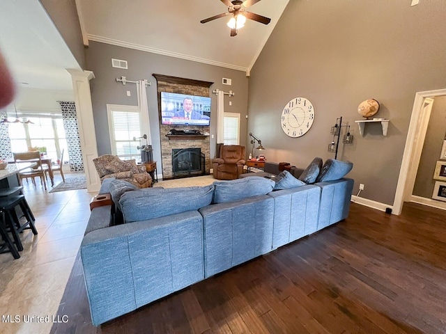 living room featuring crown molding, high vaulted ceiling, decorative columns, dark hardwood / wood-style flooring, and a stone fireplace