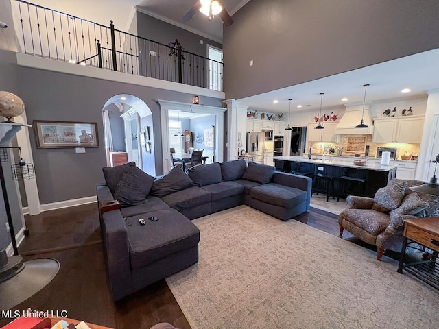 living room featuring crown molding, ceiling fan, wood-type flooring, and a high ceiling