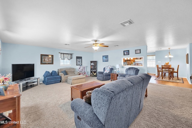 carpeted living room featuring ceiling fan with notable chandelier, a textured ceiling, and a wealth of natural light