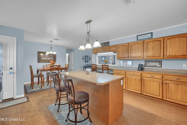 kitchen featuring a kitchen bar, a notable chandelier, light hardwood / wood-style floors, a kitchen island, and hanging light fixtures