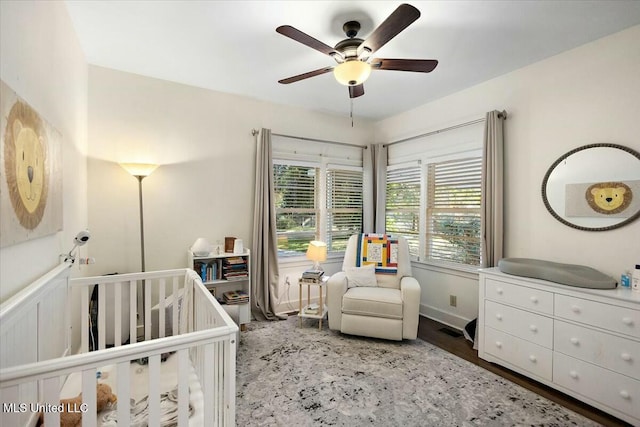 bedroom with ceiling fan, wood-type flooring, and a crib