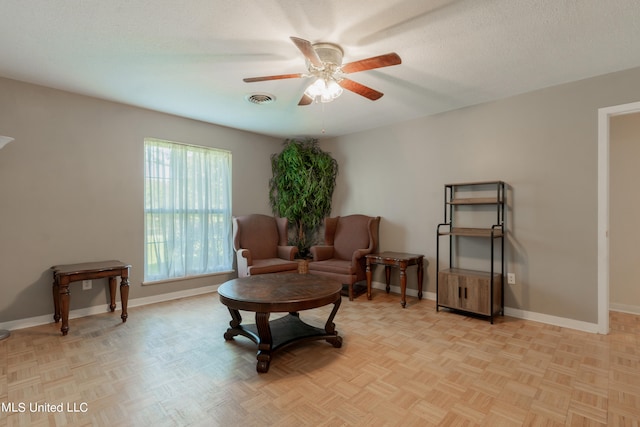 living area featuring a textured ceiling, light parquet flooring, and ceiling fan