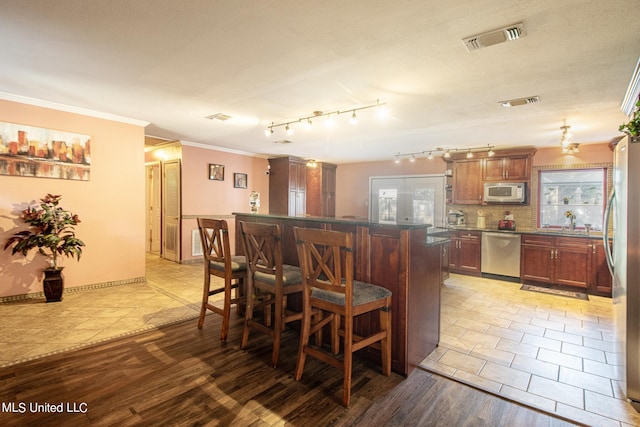 kitchen featuring light hardwood / wood-style flooring, appliances with stainless steel finishes, a wealth of natural light, and a kitchen bar