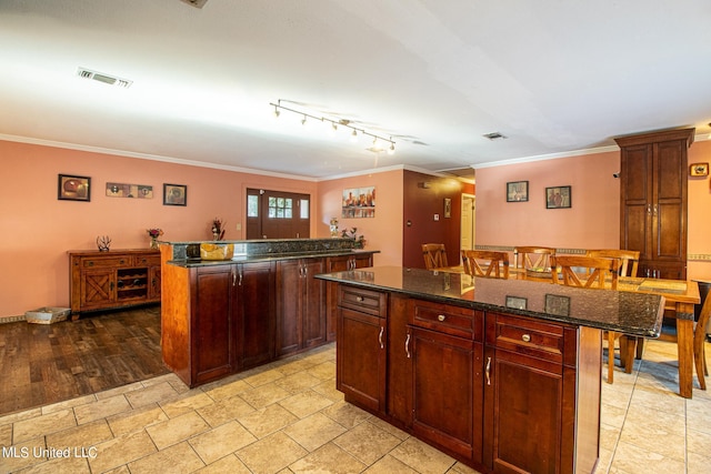 kitchen featuring a kitchen island, a kitchen bar, dark stone counters, light hardwood / wood-style flooring, and ornamental molding