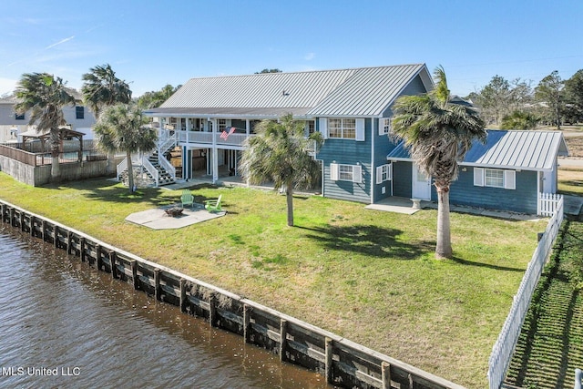 back of property featuring a water view, a yard, a fire pit, and a patio area