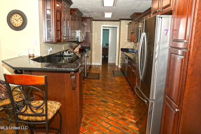 kitchen with crown molding, a textured ceiling, appliances with stainless steel finishes, a kitchen bar, and kitchen peninsula