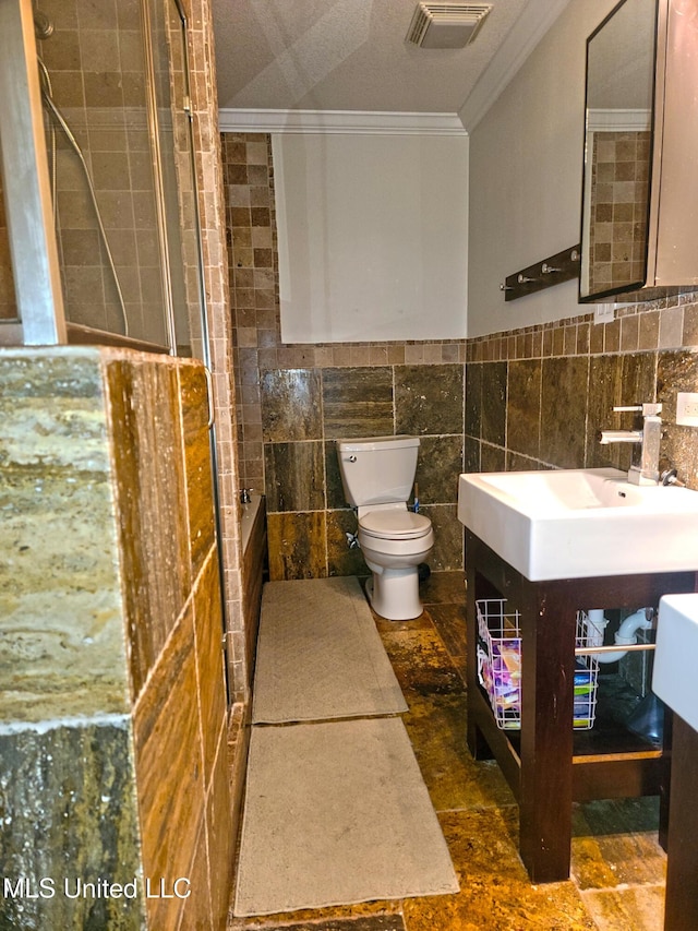 bathroom with walk in shower, crown molding, toilet, vanity, and tile walls