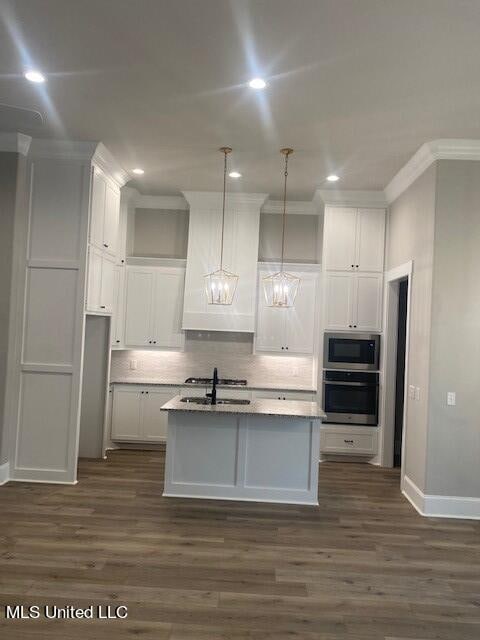 kitchen with decorative light fixtures, an island with sink, white cabinetry, sink, and stainless steel appliances