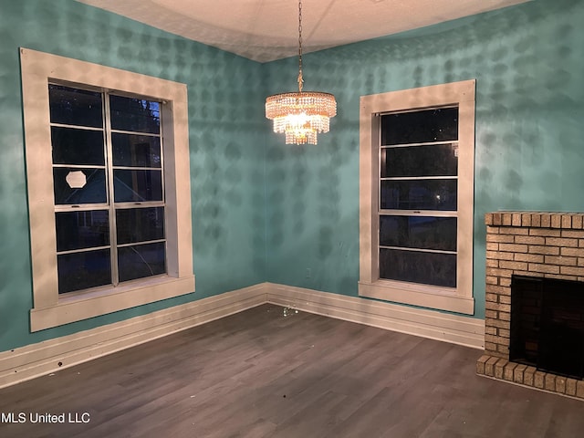 unfurnished dining area featuring a fireplace, a textured ceiling, dark hardwood / wood-style flooring, and a notable chandelier