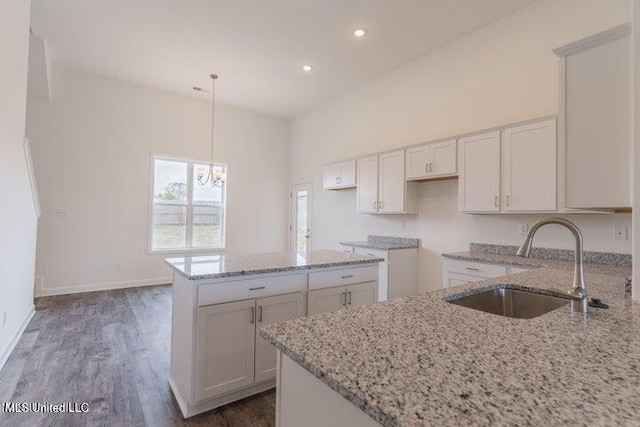 kitchen with light stone countertops, sink, a kitchen island, decorative light fixtures, and white cabinets