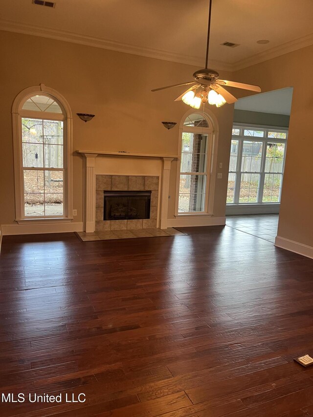 unfurnished living room with plenty of natural light, ceiling fan, dark hardwood / wood-style flooring, and a tiled fireplace