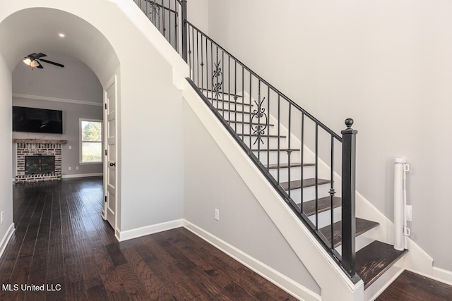 staircase featuring ceiling fan, wood-type flooring, and a brick fireplace