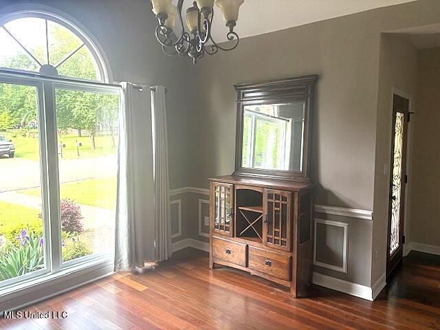 dining space with an inviting chandelier, dark wood finished floors, and a wainscoted wall