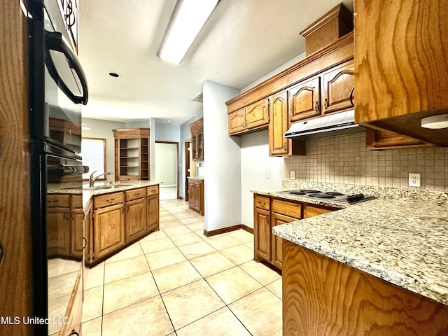 kitchen featuring brown cabinetry, backsplash, light stone countertops, and a sink