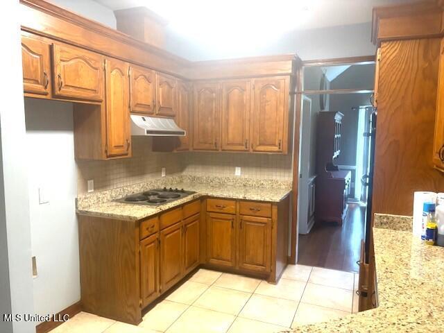 kitchen with under cabinet range hood, stainless steel stovetop, tasteful backsplash, and brown cabinets